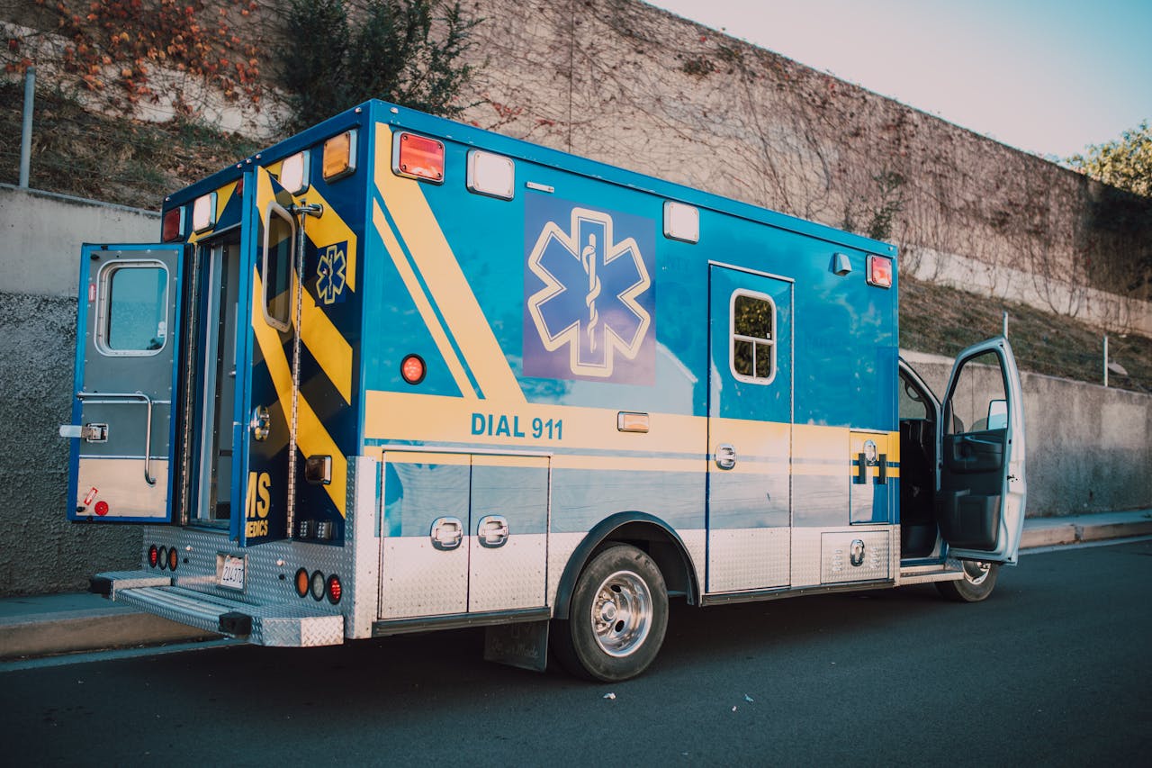 A blue ambulance with open doors parked on a sunny roadside, emergency vehicle